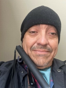 Robert smiles for a selfie; he's wearing a black cap and black jacket