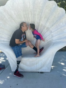 Robert Edwards sits in a large shell chair; his granddaughter leans over to give him a kiss.